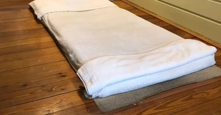 De massagemat met witte handdoeken op de houten vloer van de salon