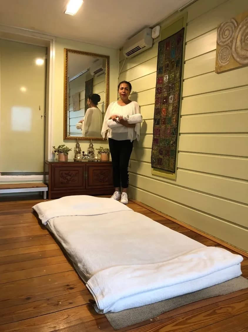 De behandelkamer van CenterCare: een massagemat met witte handdoeken op een houten vloer, met de masseuse op de achtergrond